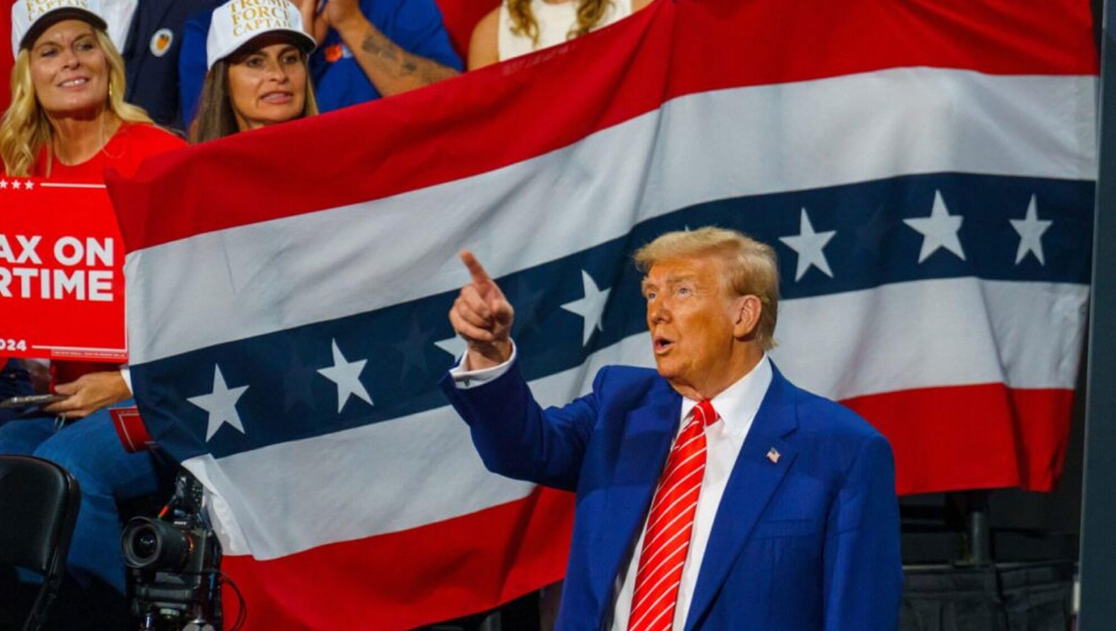 Donald Trump giving a speech to people and representing the patriotic flag in the background.