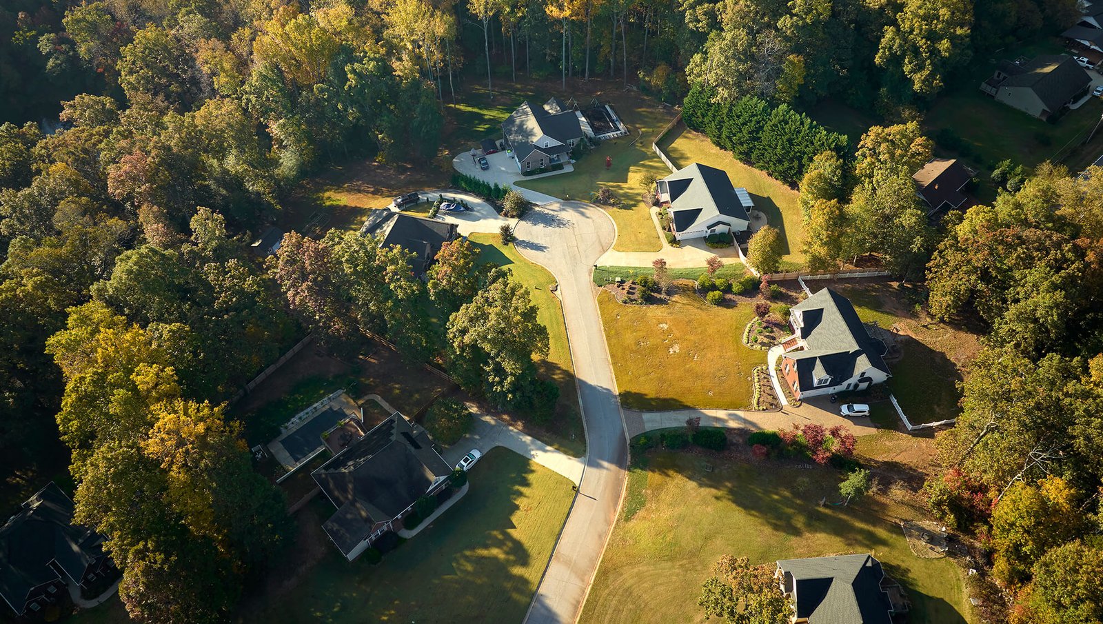 An aerial view of a suburban neighborhood featuring spacious homes, neatly maintained lawns, winding roads, and surrounding greenery.