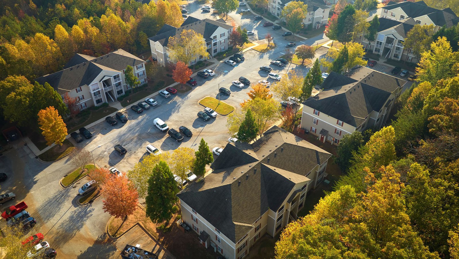 An aerial view of a residential community with multiple apartment buildings, a parking lot, and vibrant autumn trees surrounding the area.