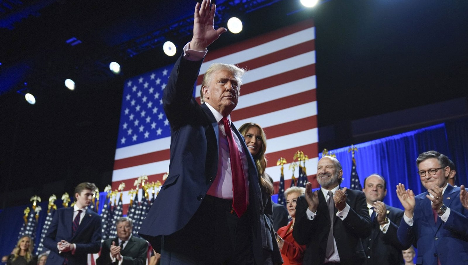 A public figure Donal Trump waves his hand to a cheering crowd on stage