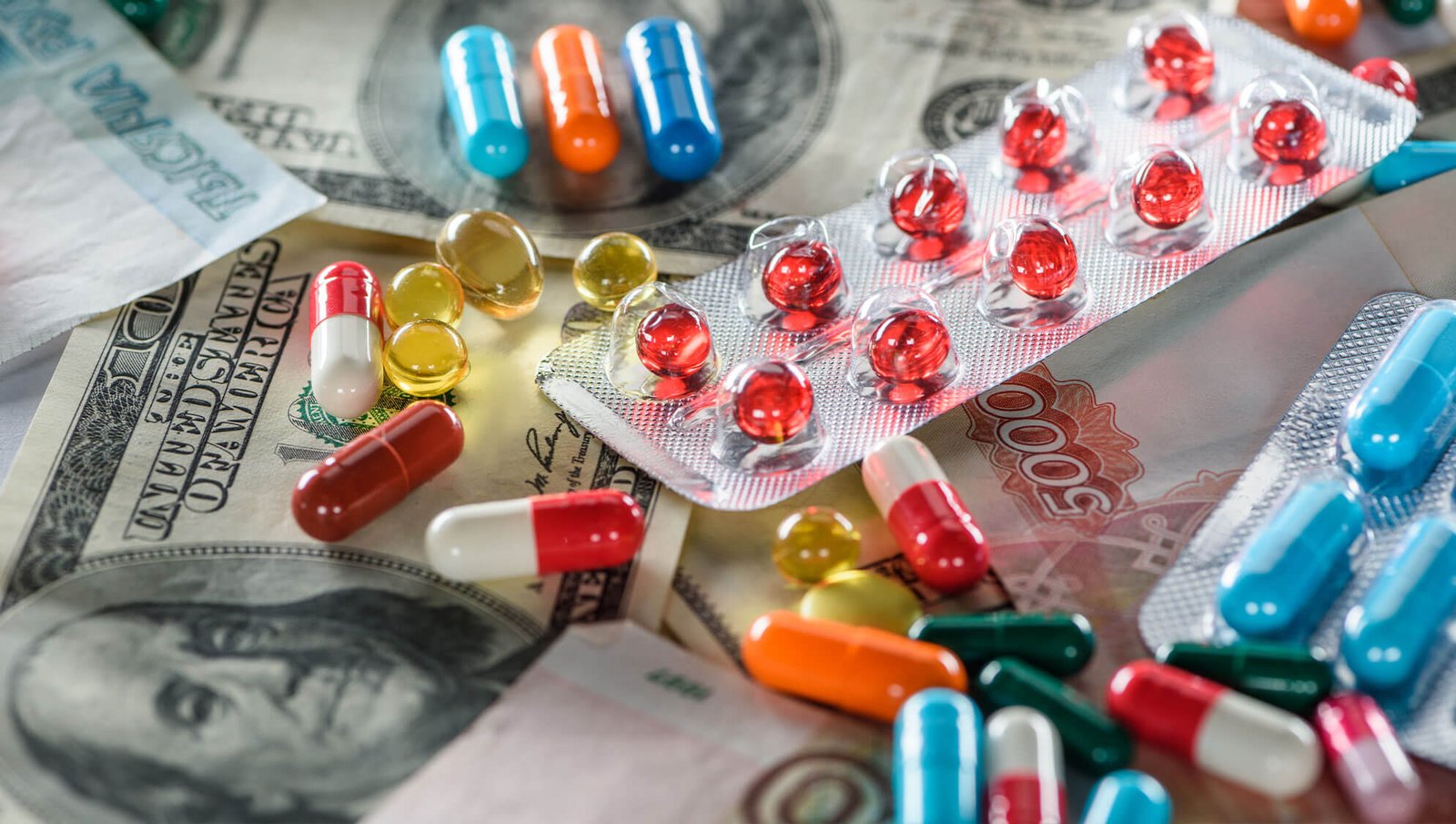 A collection of colorful pills, capsules, and blister packs placed on various currency notes, symbolizing the cost of healthcare or medicine.