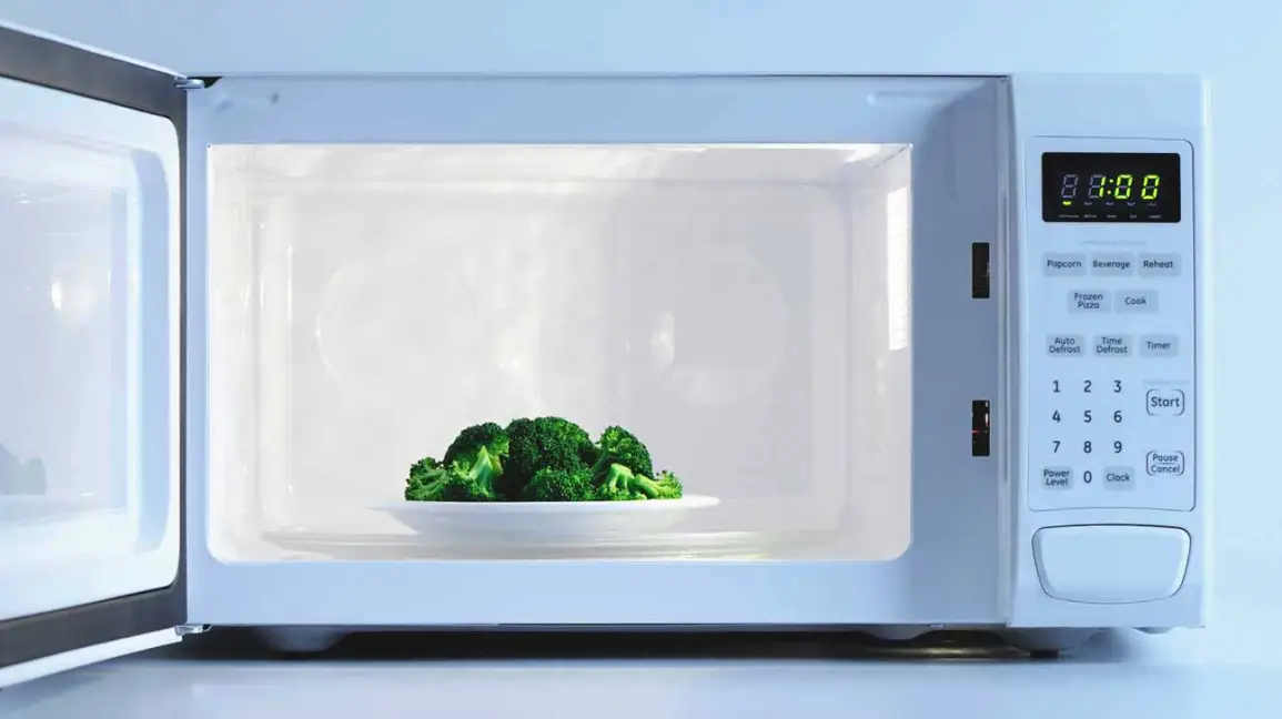 microwave with its door open, displaying a plate of steamed broccoli inside