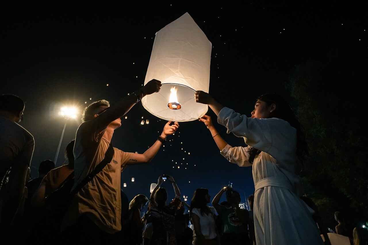 Two people releasing a glowing sky lantern into the night sky during a festival
